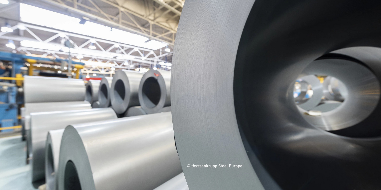 Rolled steel coils stored in an industrial production hall.