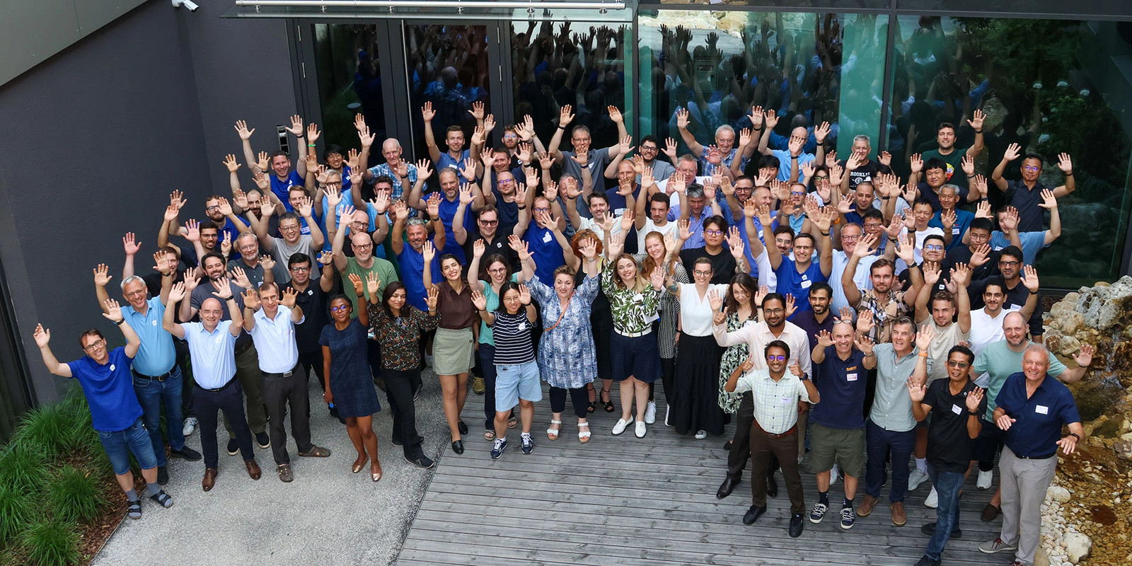 Large group of employees waving in front of a modern office building during a team gathering.