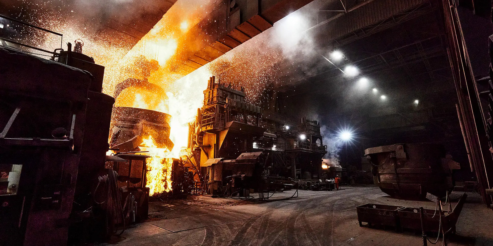 Steel plant with glowing molten metal pouring from a blast furnace inside a large industrial hall