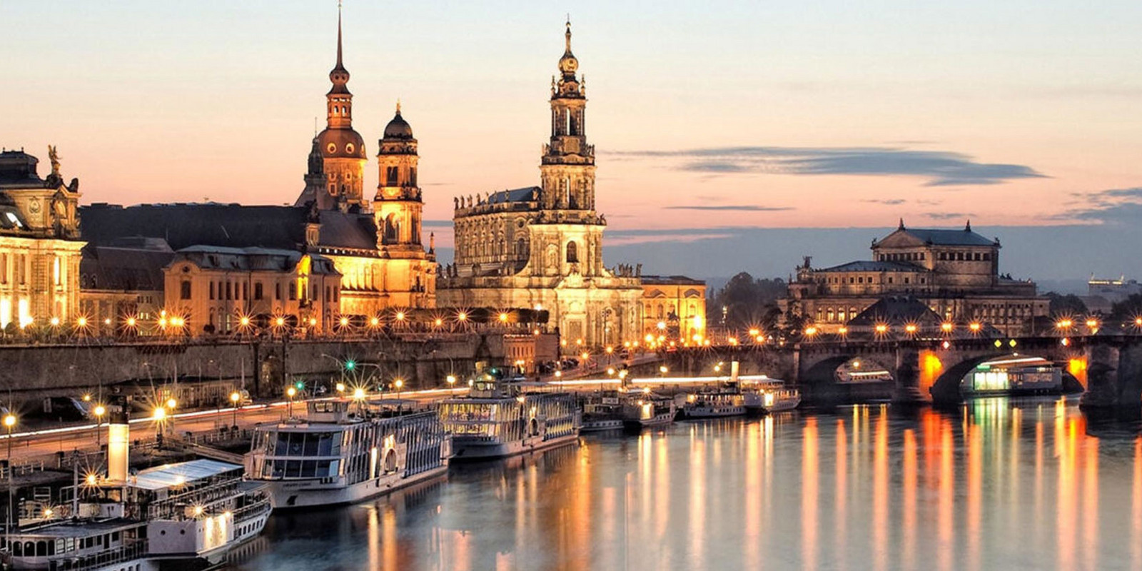 Cityscape of illuminated historic buildings along a river at sunset.