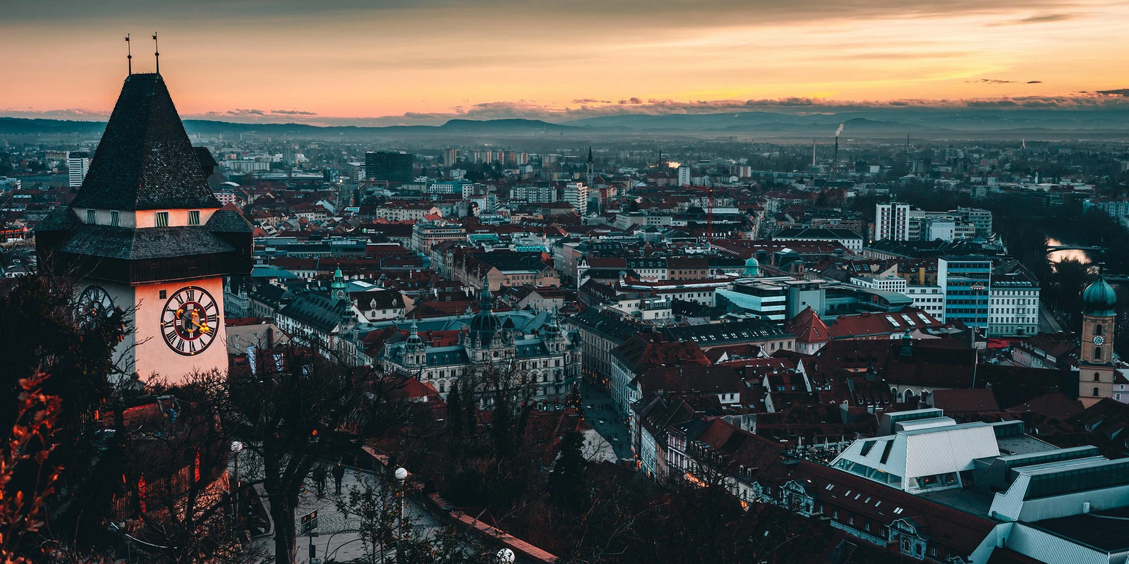 Panoramic view of Graz at sunset with the iconic clock tower overlooking the city’s rooftops.