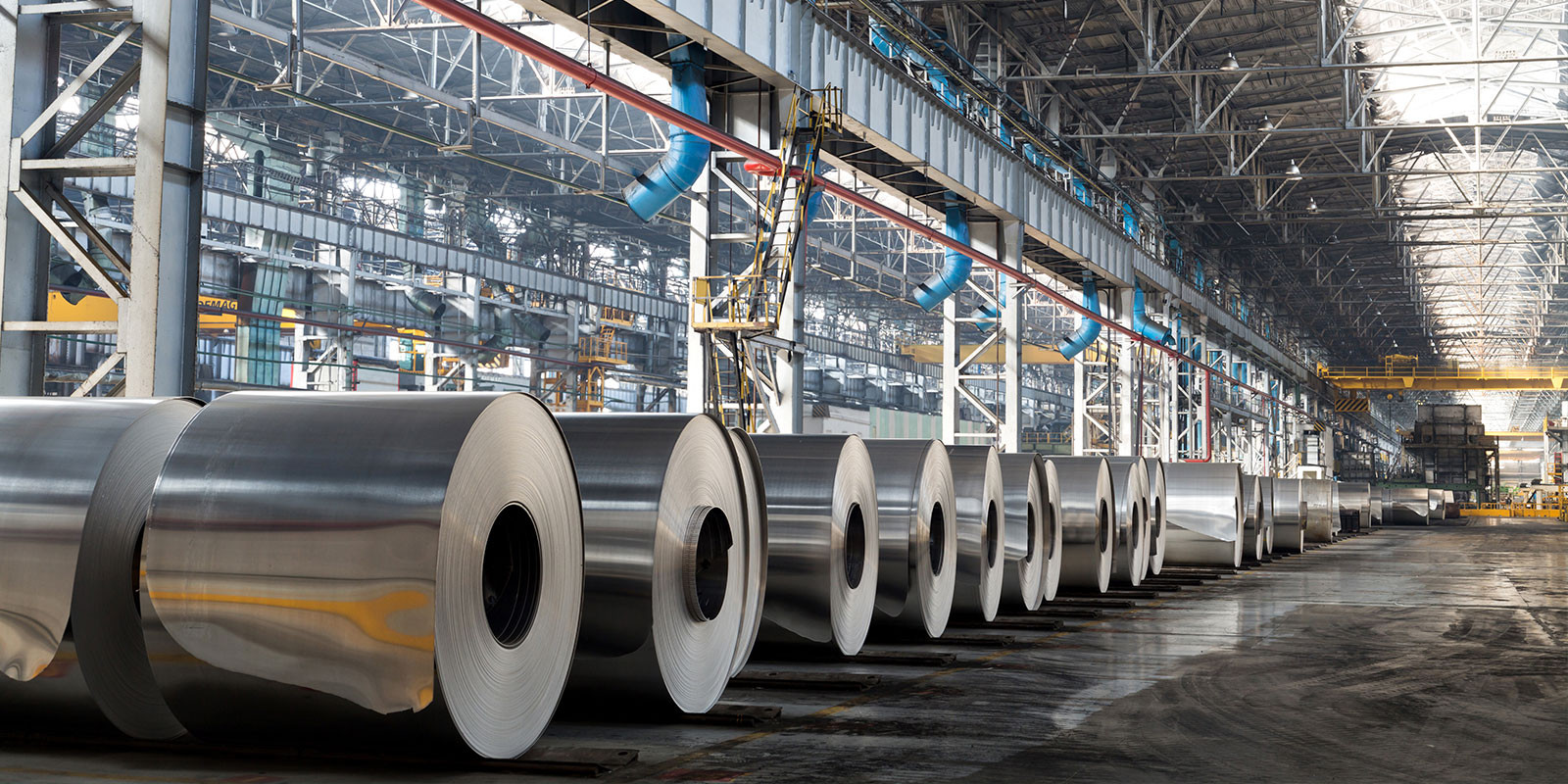 Multiple large, shiny aluminum rolls lined up in a warehouse.
