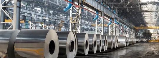 Multiple large, shiny aluminum rolls lined up in a warehouse.