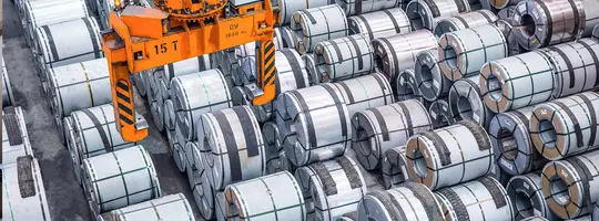 An orange 15-ton overhead crane is positioned above a massive collection of stacked steel coils.