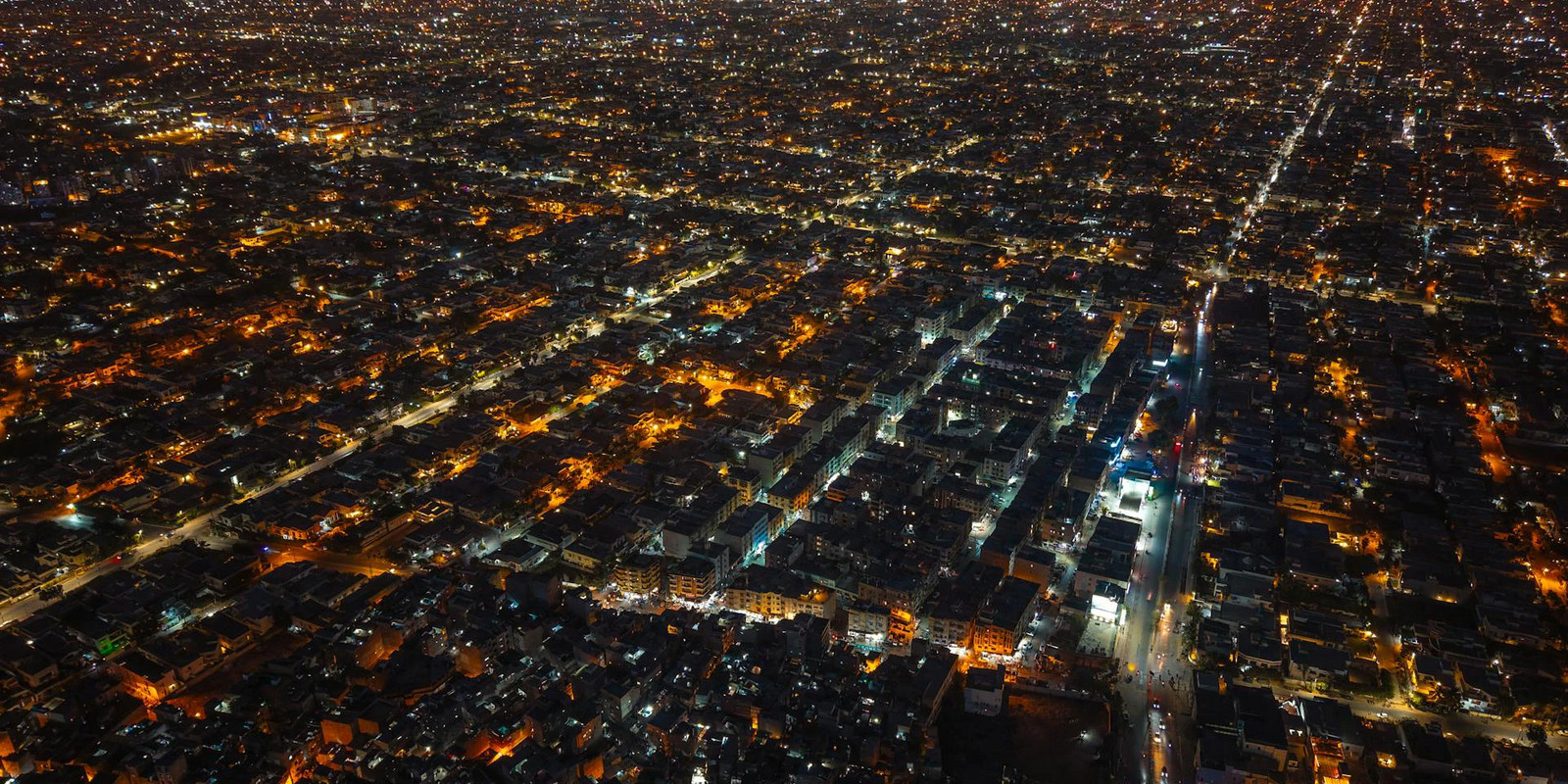 Aerial night view of a vast city with a dense grid of streets illuminated by countless lights.